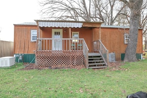 A wooden cabin with a porch, a small staircase, and a fenced yard.