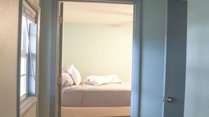 Un pasillo estrecho que conduce a un dormitorio con cama y ventana.