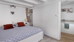 Un dormitorio con cama, mesita de noche, estante en la pared y puerta que da a un baño.