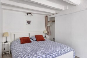 A bedroom with a bed, two bedside tables, a hanging light, a wall-mounted heart decoration, and a closet with a hanging rod.