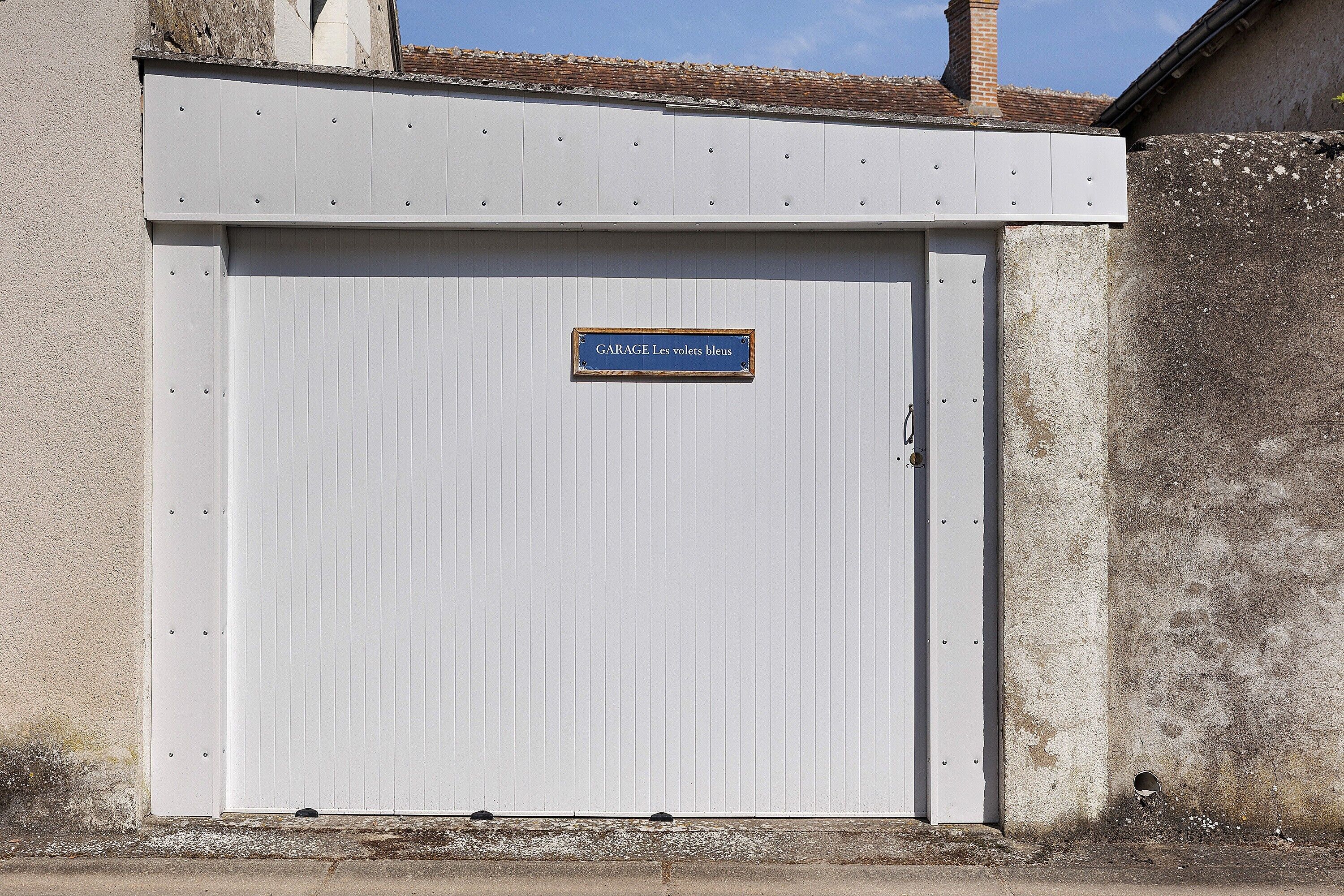 Puerta de garaje cerrada con un letrero que dice 'GARAGE Les voltes bleus'.