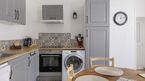 Una cocina compacta con armarios grises, lavadora, horno, cafetera y un reloj en la pared.