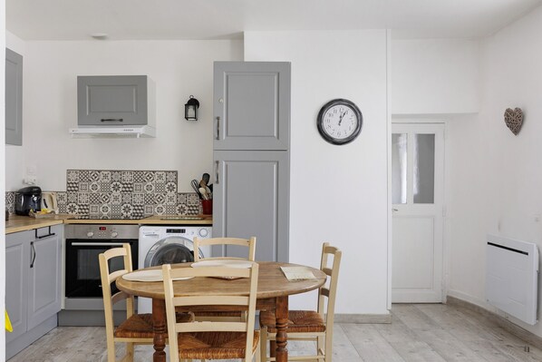 A compact kitchen with a dining table, chairs, a washing machine, and a clock on the wall.