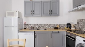 Una cocina compacta con gabinetes grises, un microondas, un refrigerador, un lavavajillas, una cafetera y una lavadora.