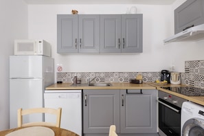 A compact kitchen with grey cabinets, a microwave, a refrigerator, a dishwasher, a coffee maker, and a washing machine.