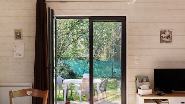 A room with a sliding glass door leading to a garden, a white TV stand with a flat-screen TV, and a dining area with a table and chairs. - Gîte Nature and Spa - Oisly (Oisly)