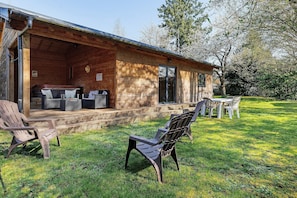 Une cabane en bois avec un porche, un espace salon extérieur et une cour gazonnée.