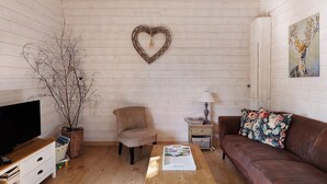 A cozy living room with a heart-shaped wall decoration, a television, a brown leather sofa, a wooden coffee table, and a side table with a lamp. - Gîte Nature and Spa - Oisly (Oisly)