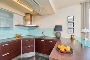 A modern kitchen with dark wooden cabinets, a glass countertop, and a sink. There is a bowl of oranges on the counter and a lamp on the right side. - Hedera Estate, Villa Hedera XXIV (Zaton Mali)