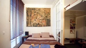 A bedroom with a bed, a painting, a window with blinds, and a bookshelf. - Bien situe (Paris)