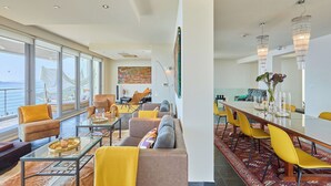A spacious living area with a large window overlooking a scenic view, a dining area with a long table and yellow chairs, and a cozy seating area with sofas and a coffee table. - Hedera Estate, Villa Hedera XXII (Zaton Mali)