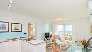 Een moderne keuken met witte kastjes, een spoelbak en een eethoek met een tafel en stoelen. Er is een groot raam met uitzicht op zee.