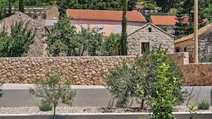 Un muro de piedra, un pequeño árbol y un edificio con techo rojo.