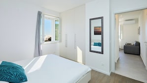 Un dormitorio con cama, ventana, armario, espejo y puerta que da a otra habitación.