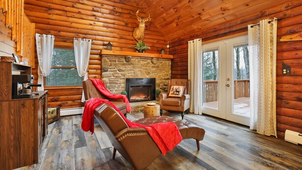 A log cabin interior with a stone fireplace, leather recliners, a ceiling fan, and a view through a glass door. - Secluded Poconos Log Cabin - Hot tub, Fire Pit, Game Room (Greene Township)