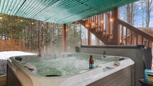 A hot tub with a wooden deck and a metal roof, surrounded by trees. - Secluded Poconos Log Cabin - Hot tub, Fire Pit, Game Room (Greene Township)