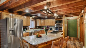 A kitchen with wooden cabinets, a stainless steel refrigerator, a marble countertop, and a green door. - Secluded Poconos Log Cabin - Hot tub, Fire Pit, Game Room (Greene Township)