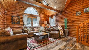 A log cabin interior with a wooden ceiling, a sofa set, a coffee table, and a large window. - Secluded Poconos Log Cabin - Hot tub, Fire Pit, Game Room (Greene Township)
