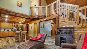 A spacious loft-style living area with a high ceiling, wooden beams, a dining area, and a kitchen with modern appliances. - Secluded Poconos Log Cabin - Hot tub, Fire Pit, Game Room (Greene Township)
