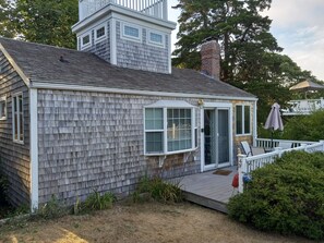 Une petite maison avec une terrasse, un porche couvert et une cheminée.