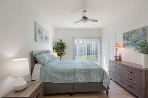 Ein Schlafzimmer mit Bett, Nachttischlampe, Schminktisch, Deckenventilator und einem Fenster mit Vorhängen.