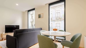 Ein modernes Wohnzimmer mit einer Couch, zwei Sesseln, einem Fernseher und einem Esstisch.