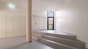 Ein geräumiges, modernes Interieur mit einer zentralen Treppe, einer Säule und einer Tür zu einem Außenbereich.