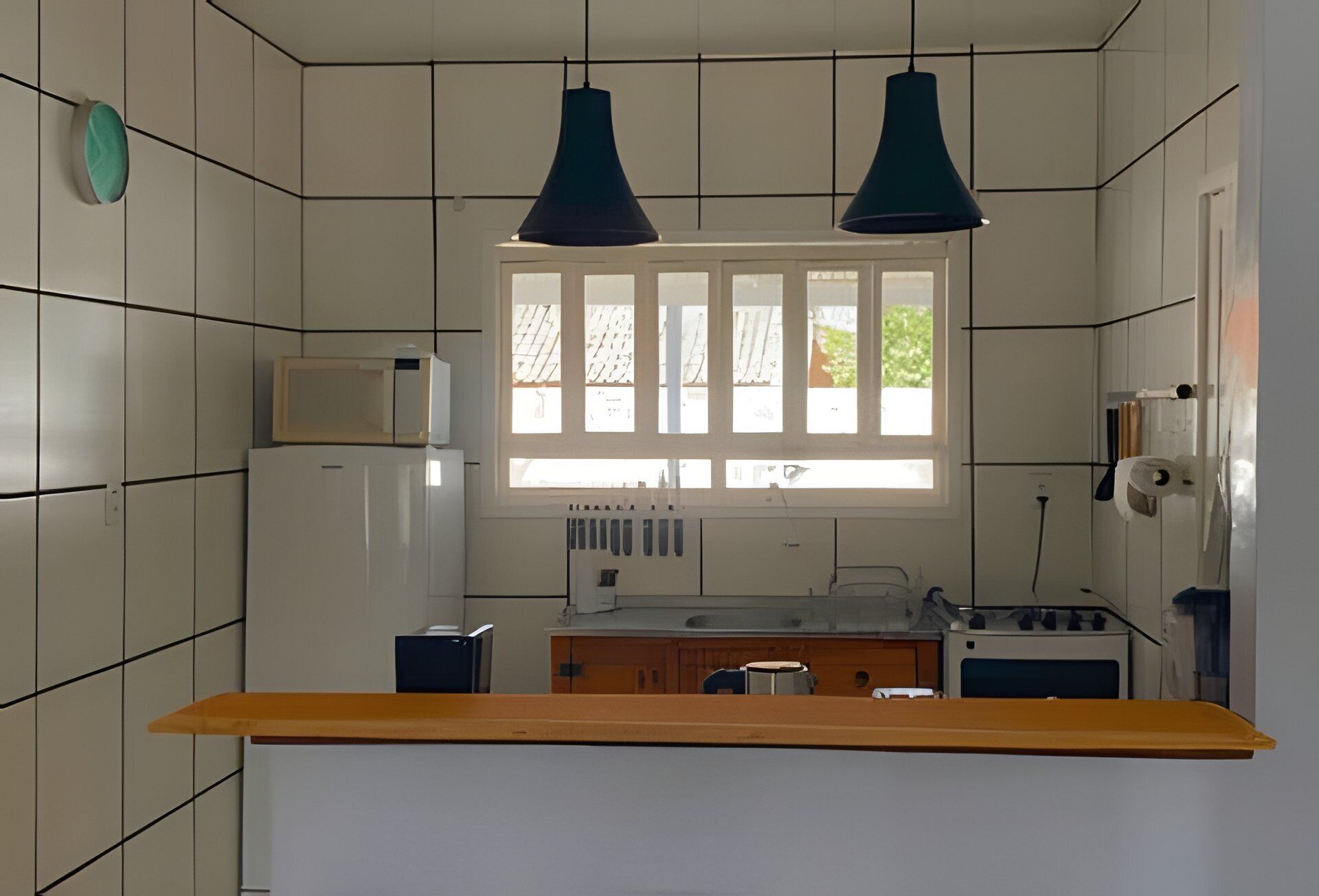 Una cocina con paredes de azulejos blancos, un ventanal con persianas, una encimera de madera y dos lámparas colgantes.