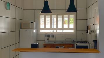 Una cocina con paredes de azulejos blancos, un ventanal con persianas, una encimera de madera y dos lámparas colgantes.