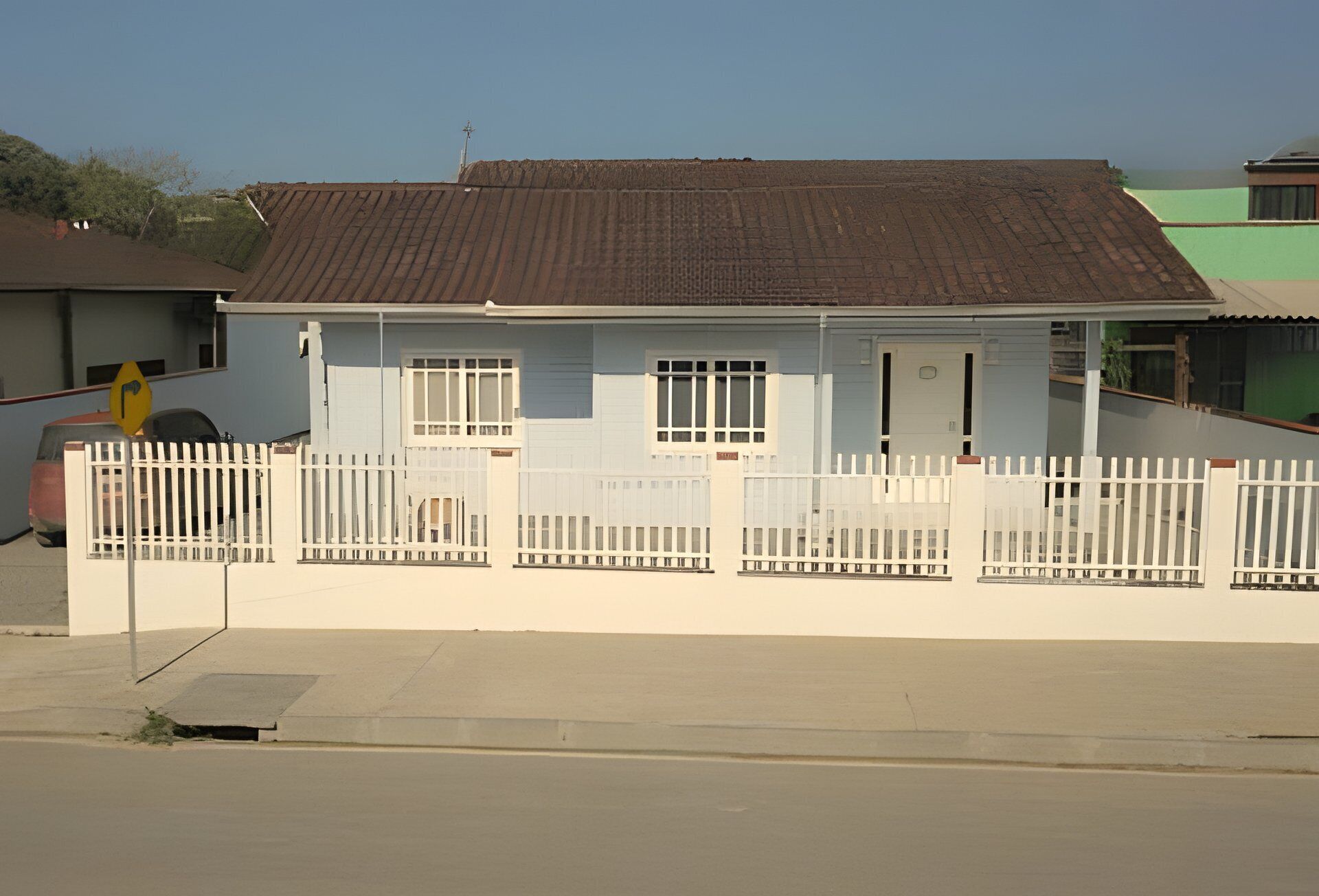 Een gelijkvloers huis met een plat dak, witte buitenmuren en een witte picket hek.
