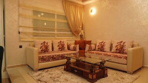 A living room with a beige sofa set, a glass coffee table, and a patterned rug. - Sky Fès Centre-ville | Moderne &
Calme | Parking (Fès)