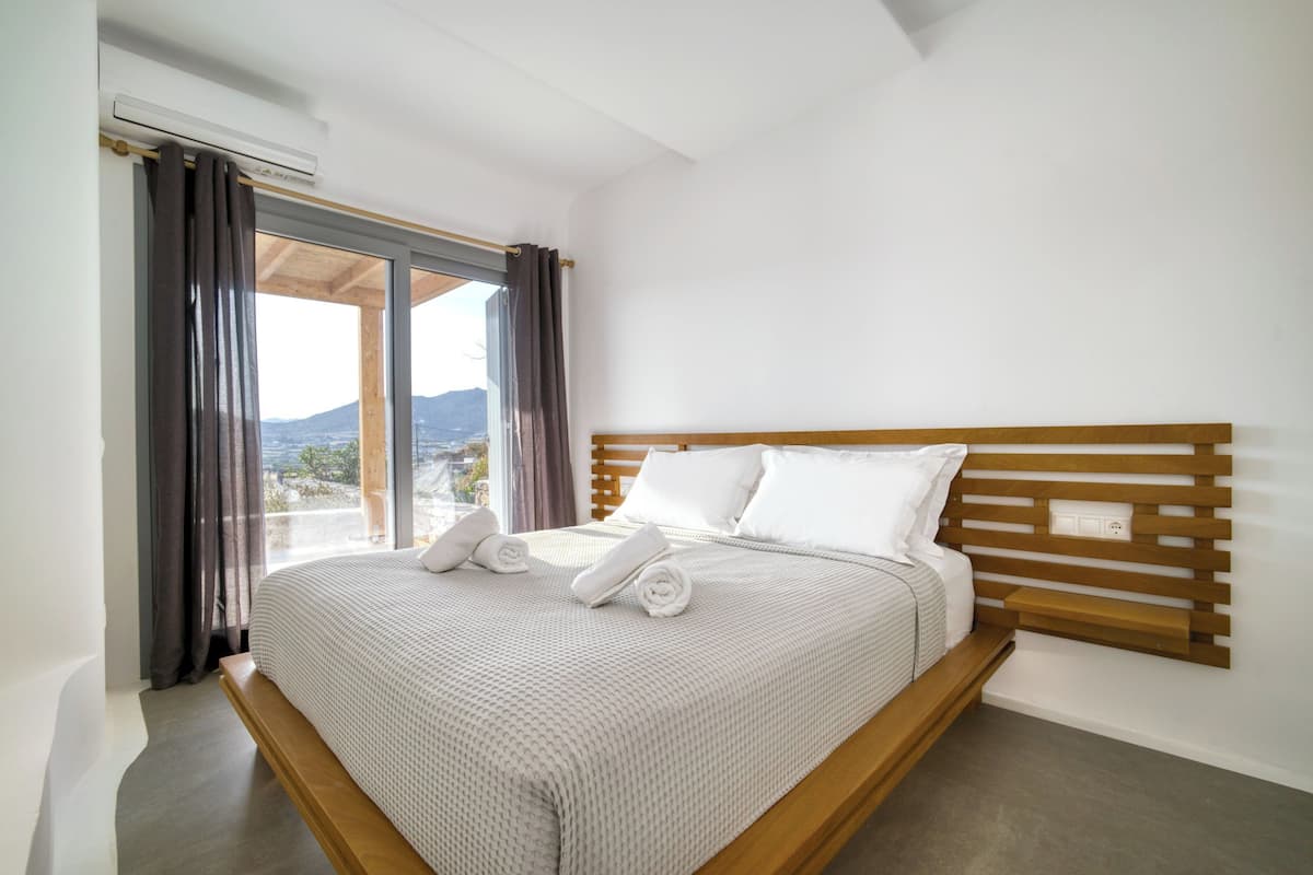 A modern bedroom with a large bed, wooden headboard, and a view of the outdoors.