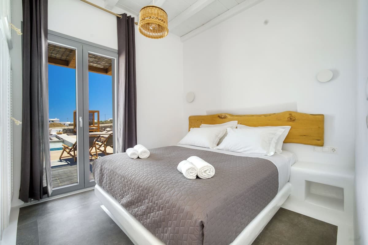 A bedroom with a large bed, a wooden headboard, and a view of an outdoor pool area through a sliding glass door.