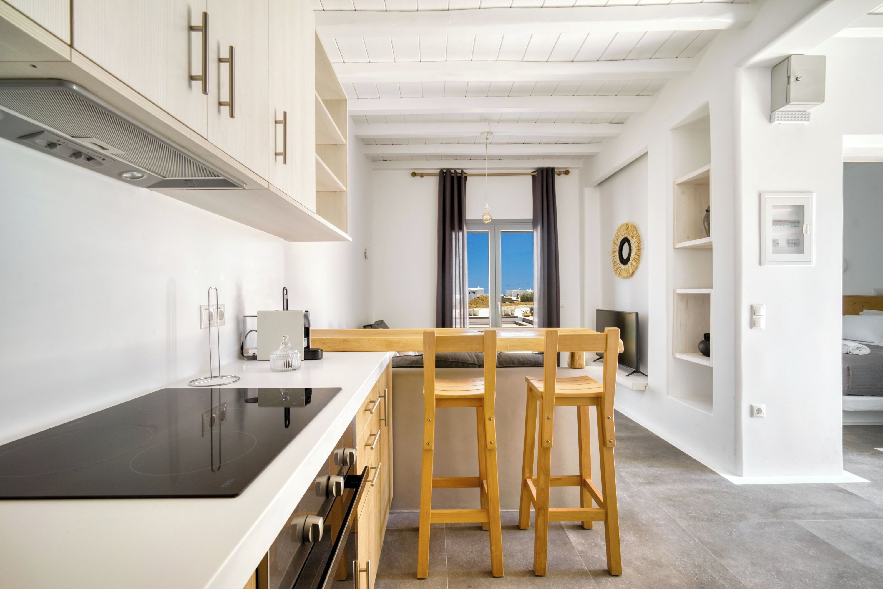 A modern kitchen with white cabinetry, a black induction cooktop, and wooden bar stools.