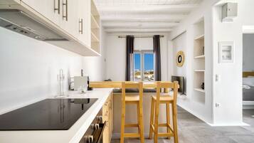 A modern kitchen with white cabinetry, a black induction cooktop, and wooden bar stools.