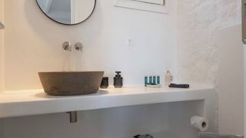 A modern bathroom with a round mirror, a window, and a toilet.