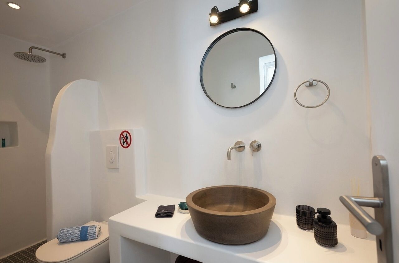 Un baño moderno con un lavabo de madera redondo, un espejo redondo y un cabezal de ducha.