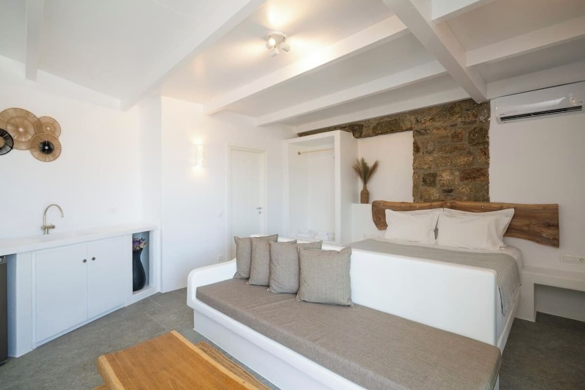 A modern bedroom with a large bed, a built-in bench, a stone accent wall, and a white wardrobe.