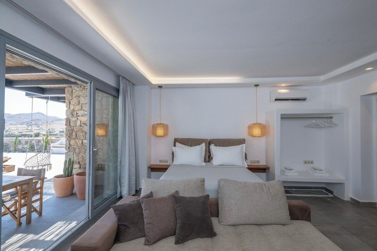 A modern bedroom with a large bed, two bedside tables, a sofa, and a view of the outdoors.