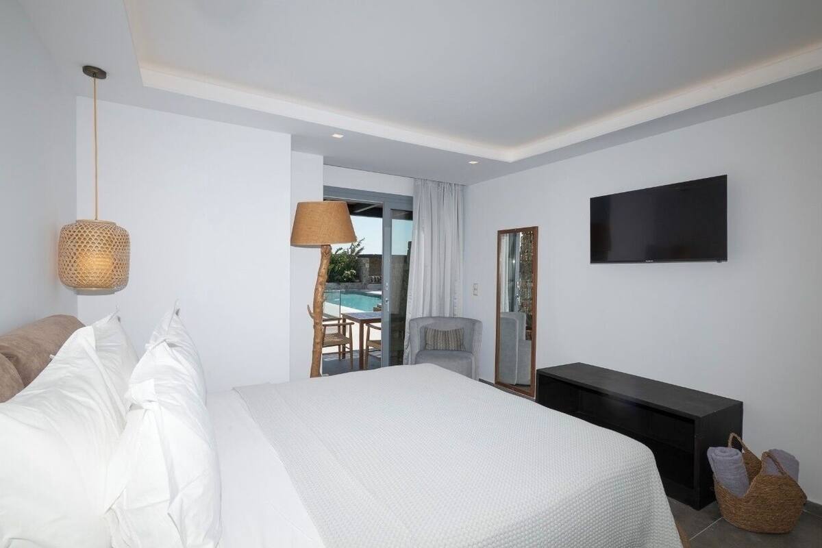 A modern hotel room with a large bed, a flat-screen TV, a bedside table, and a view of an outdoor pool area.