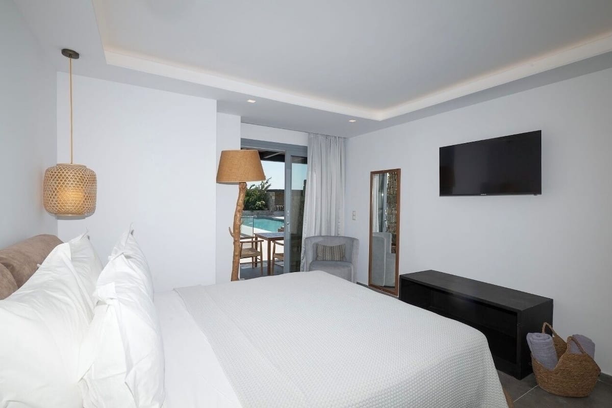 A modern hotel room with a large bed, a flat-screen TV, a bedside table, and a view of an outdoor pool area.