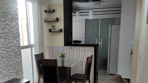 Ett modernt vardagsrum med en soffa, ett matbord med stolar och en köksdel med kylskåp och skåp.
