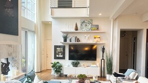 A spacious living room with a large grey sectional sofa, a flat-screen TV, and a modern chandelier. - Sublime 3 BDRM with stunning features and plunge pool in heart of Old 4th Ward! (Atlanta)