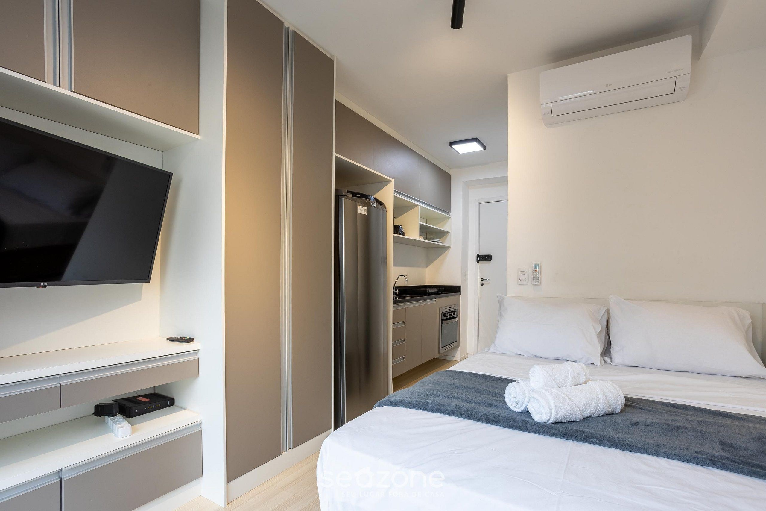Et hotelværelse med seng, fladskærms-tv, tekøkken og walk-in closet.