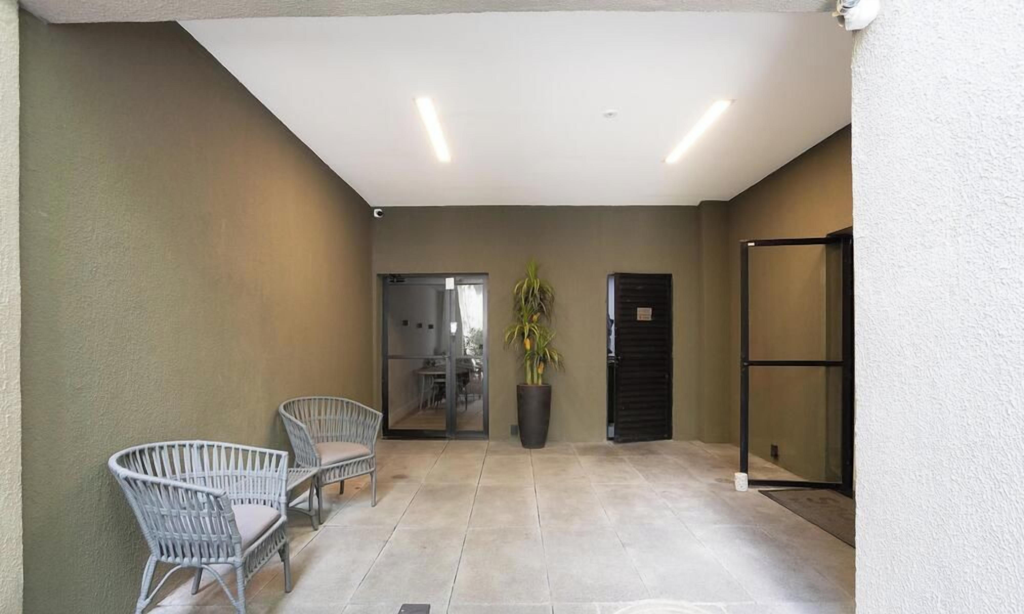 A covered outdoor area with two wicker chairs, a potted plant, and a sliding door leading to an interior space.