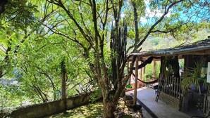 A lush garden with a pergola, stone pathway, and a rustic building with a tiled roof. - Chácara dos Cheiros: A cozy corner to relax. (Atibaia)