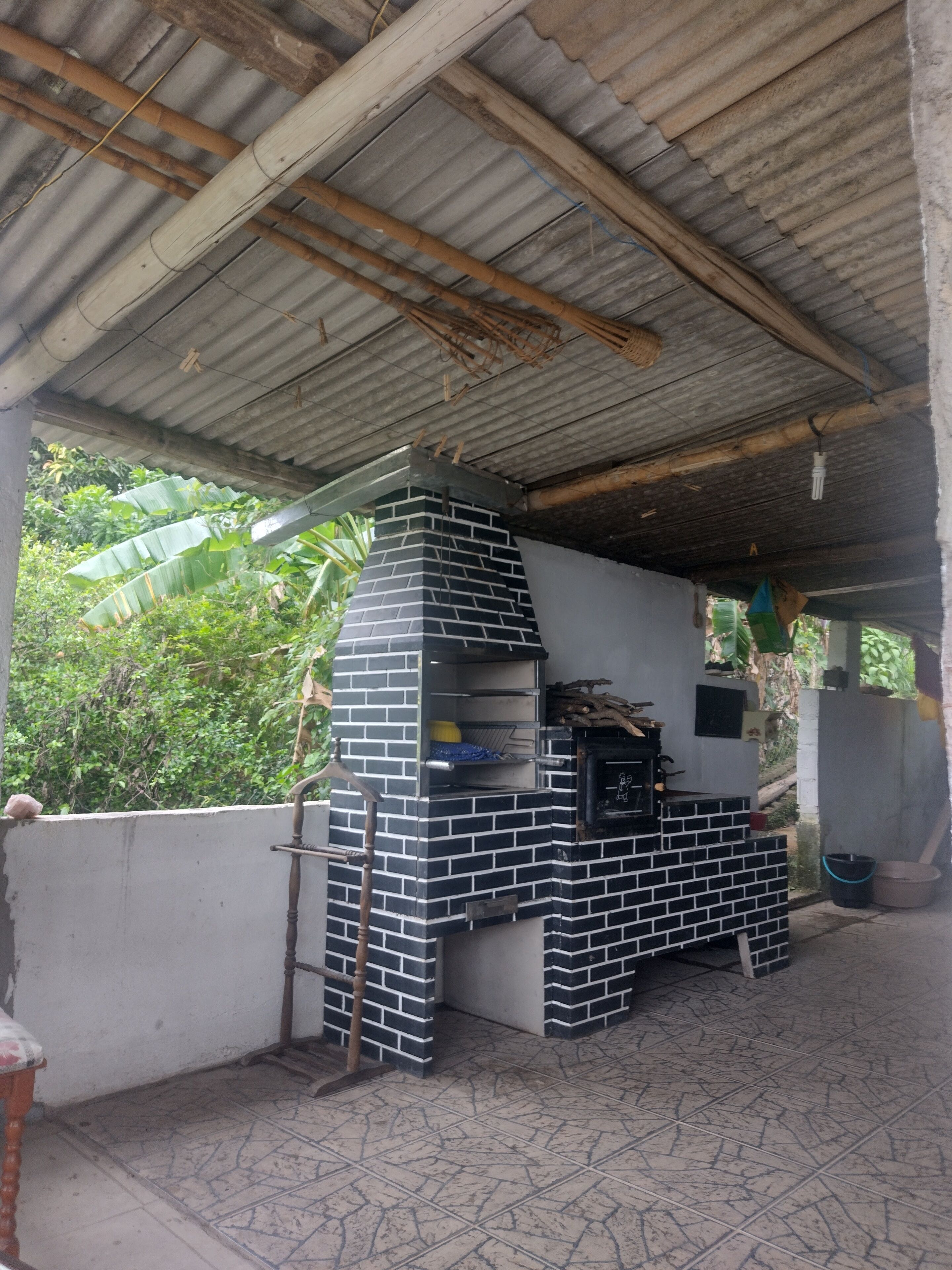 An outdoor brick oven structure with a tiled floor, surrounded by a corrugated metal roof and a concrete wall.