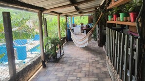 A covered outdoor area with a hammock, potted plants, and a view of a pool. - Chácara dos Cheiros: A cozy corner to relax. (Atibaia)