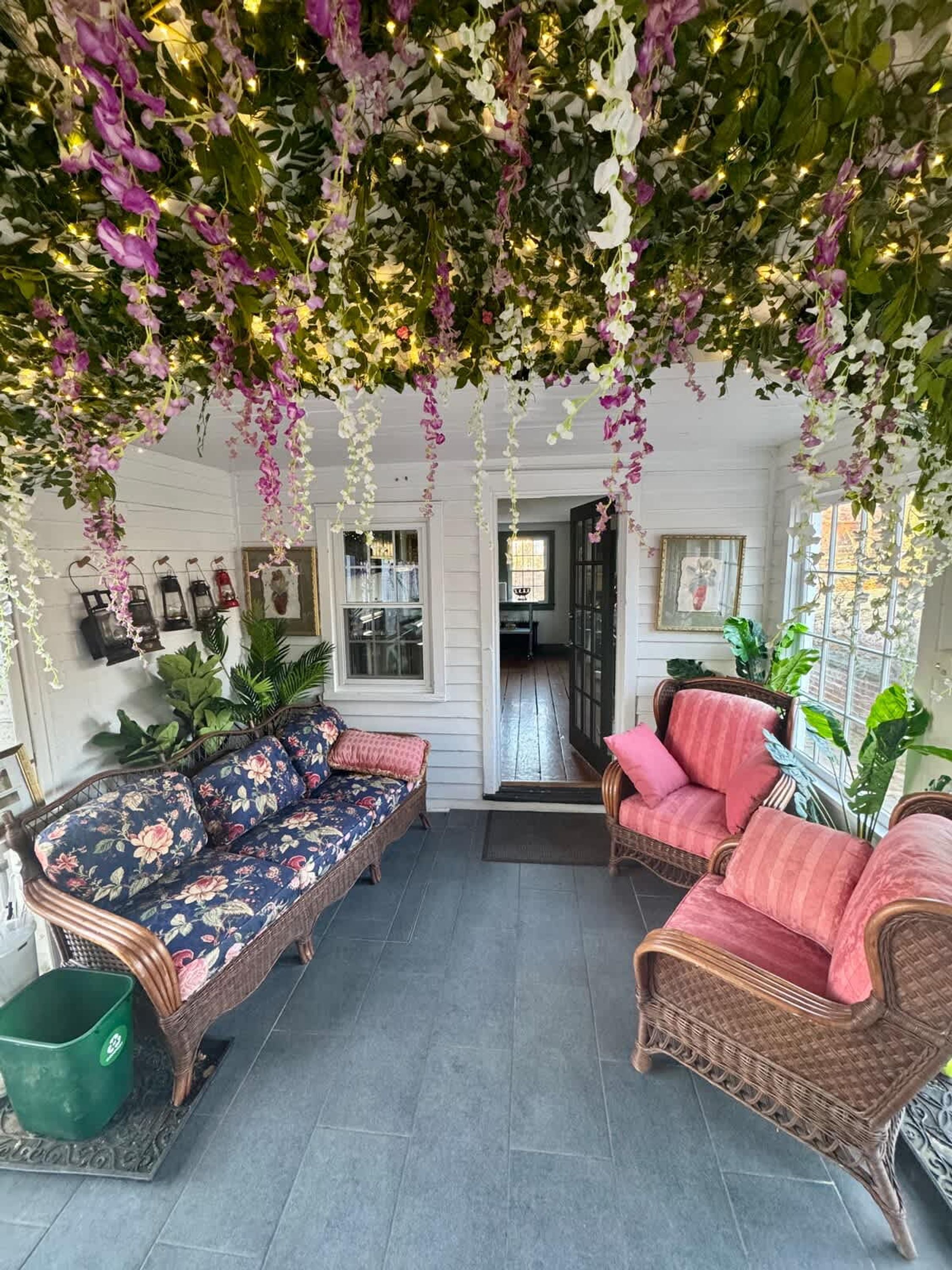 Una habitación acogedora con muebles de mimbre, adornos florales colgantes y vista al interior.