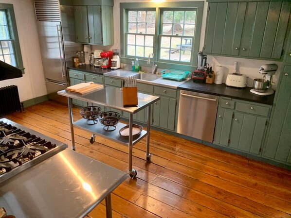 A kitchen with wooden flooring, green cabinets, a stainless steel stove, and a rolling cart with bowls. - Historic Canal Home on Nature Preserve (Princeton)